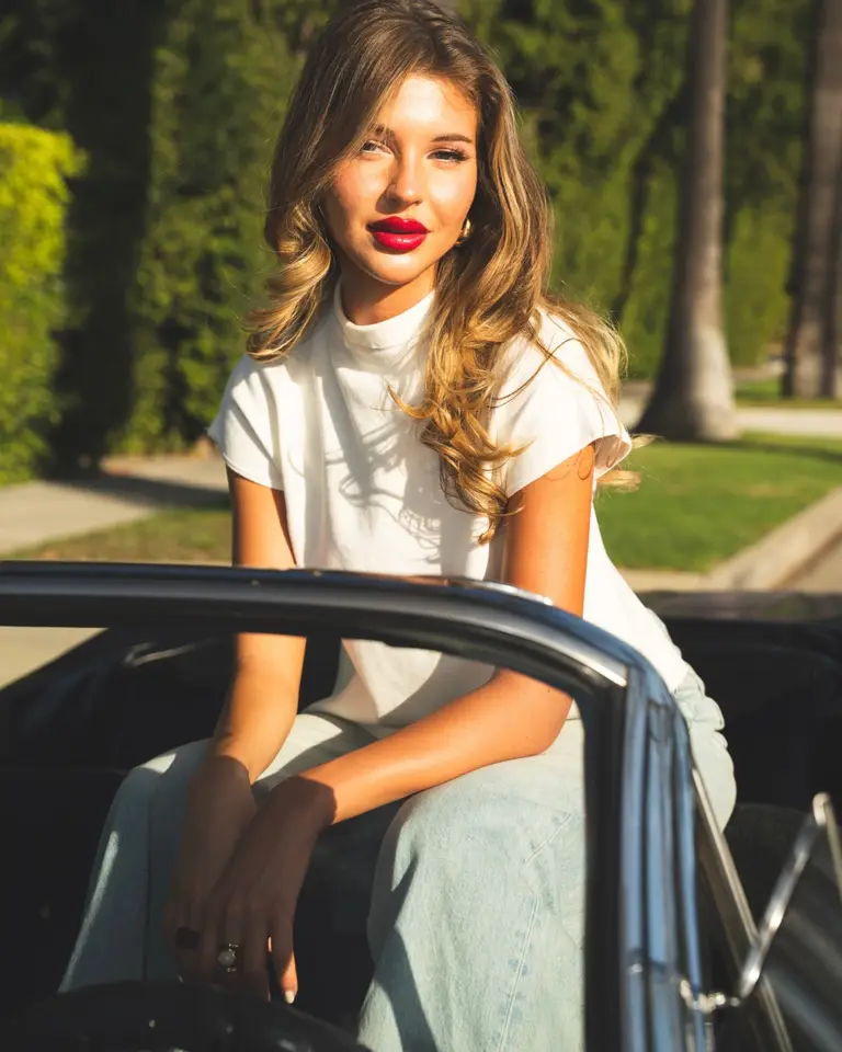 Nina, founder of Sante Organics, sitting on a vintage convertible on a palm-lined Los Angeles street