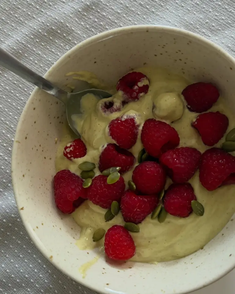 Pale green pistachio gelato topped with raspberries in a speckled ceramic bowl